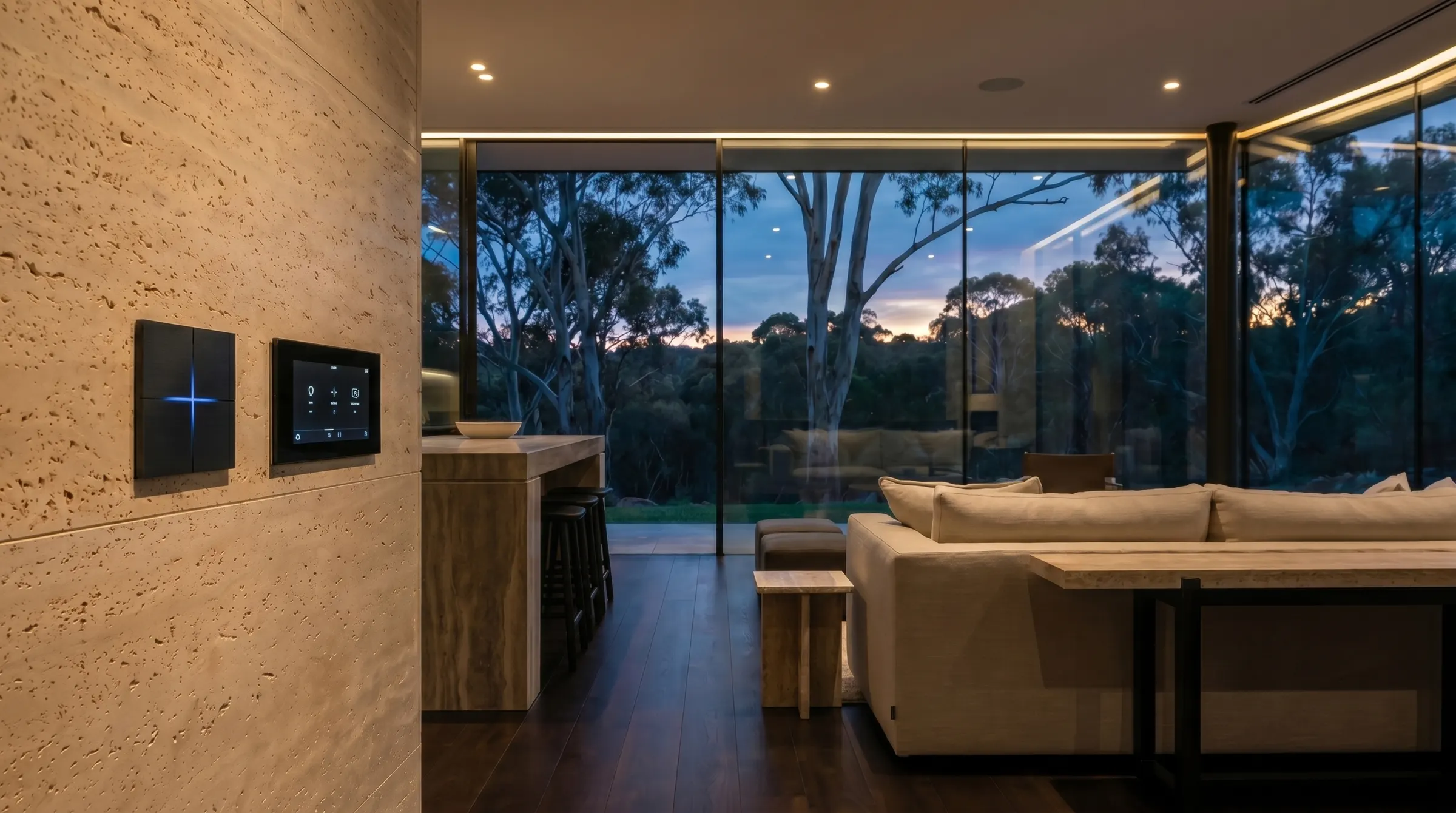 A premium Canberra living room at dusk with a real Basalte switch and touch panel on a travertine wall and gum trees beyond